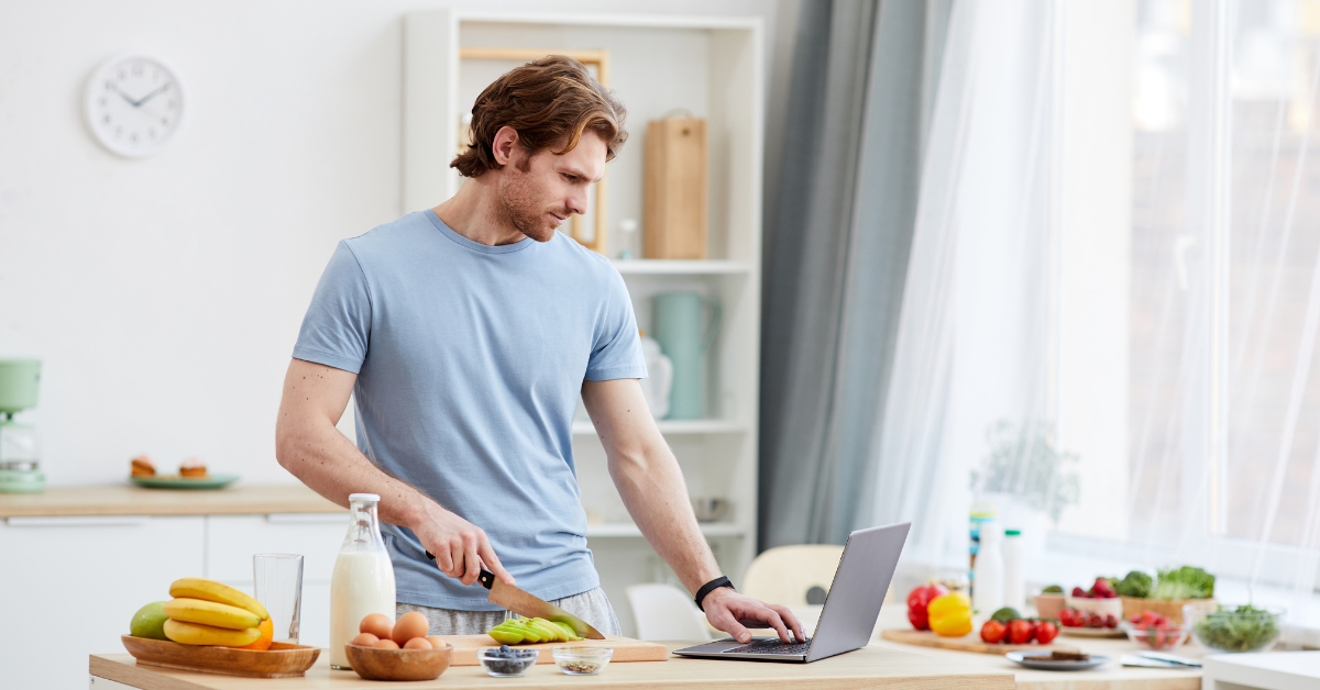 A man cooking while using a laptop